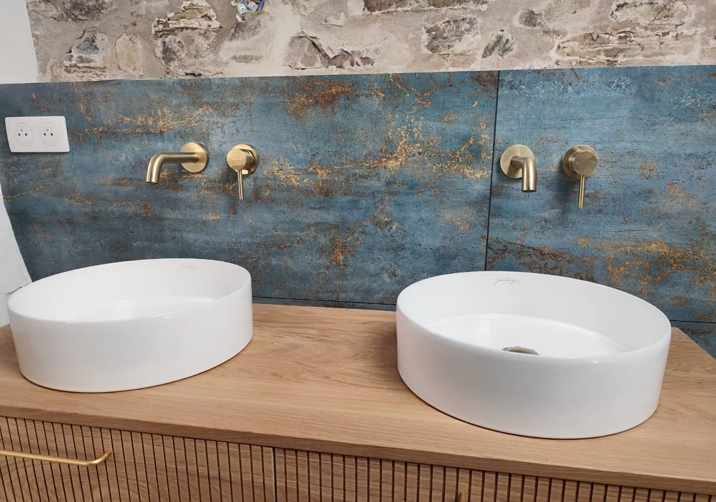 Double vasque avec crédence effet métal oxydé, robinetterie murale laiton, meuble cannelé et mur en pierre apparente conservé