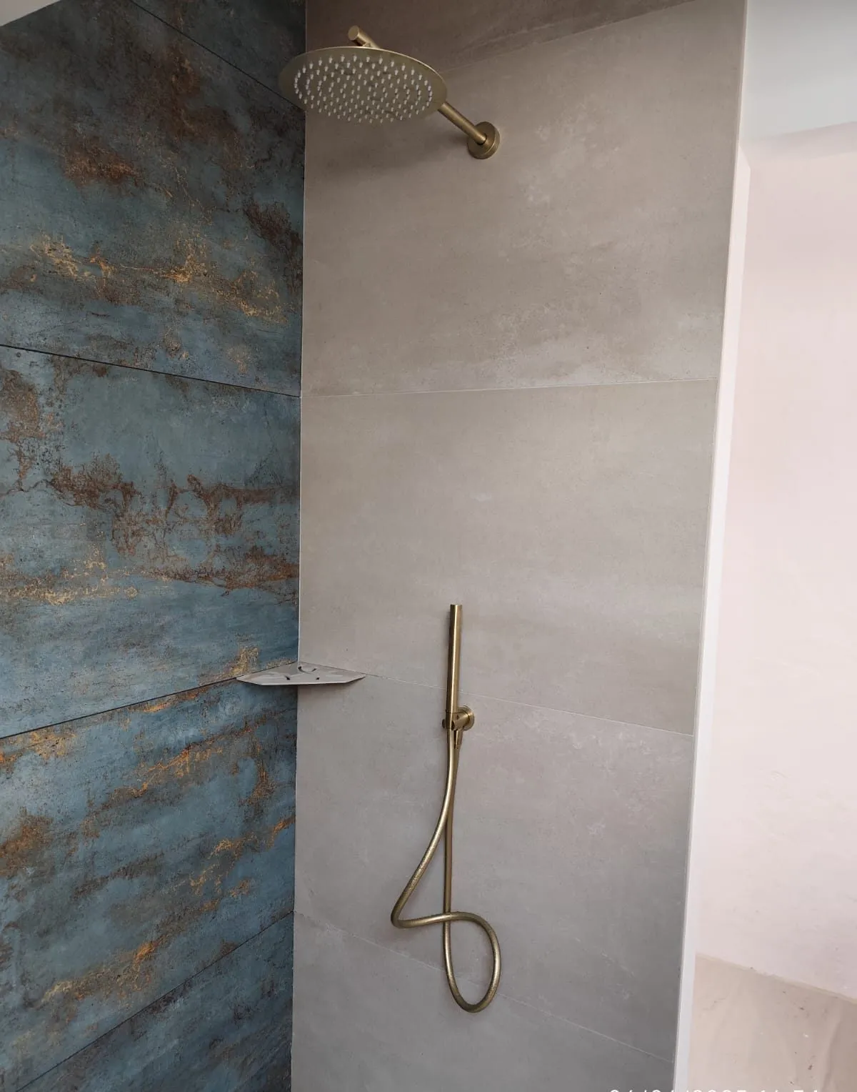Douche à l'italienne habillée d'un carrelage effet métal oxydé bleu et or, avec ciel de pluie et colonne en laiton brossé