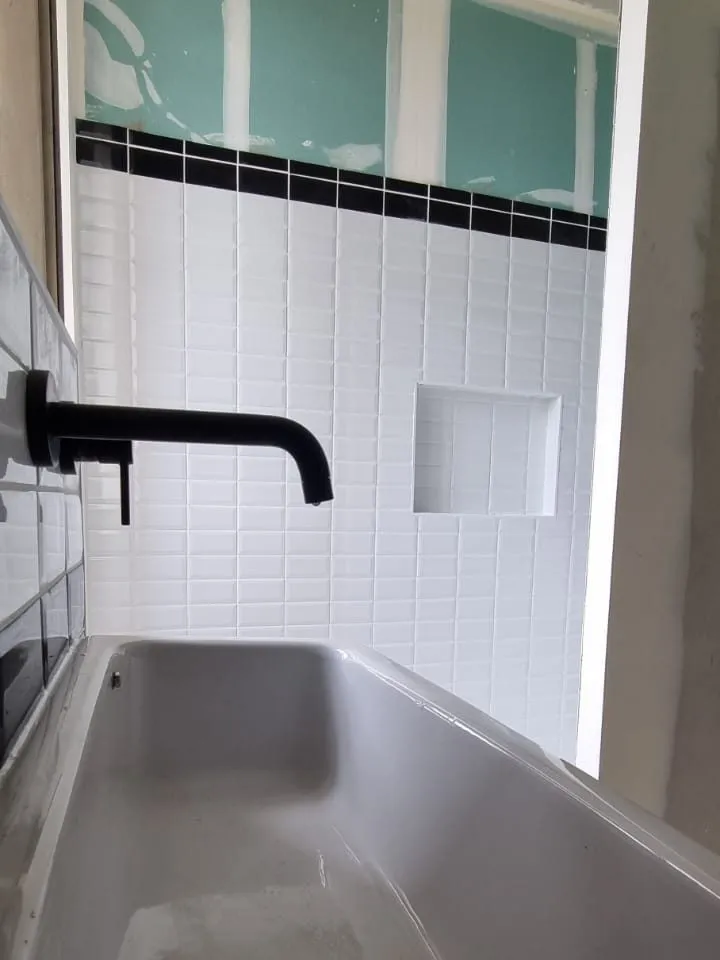 Évier inox et mitigeur mural noir posés sur un mur en carrelage métro, avec plaque de plâtre hydrofuge visible au-dessus