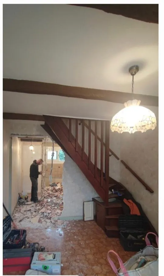Le même séjour avant travaux : escalier bois vernis, papier peint ancien, tomettes et gravats de démolition
