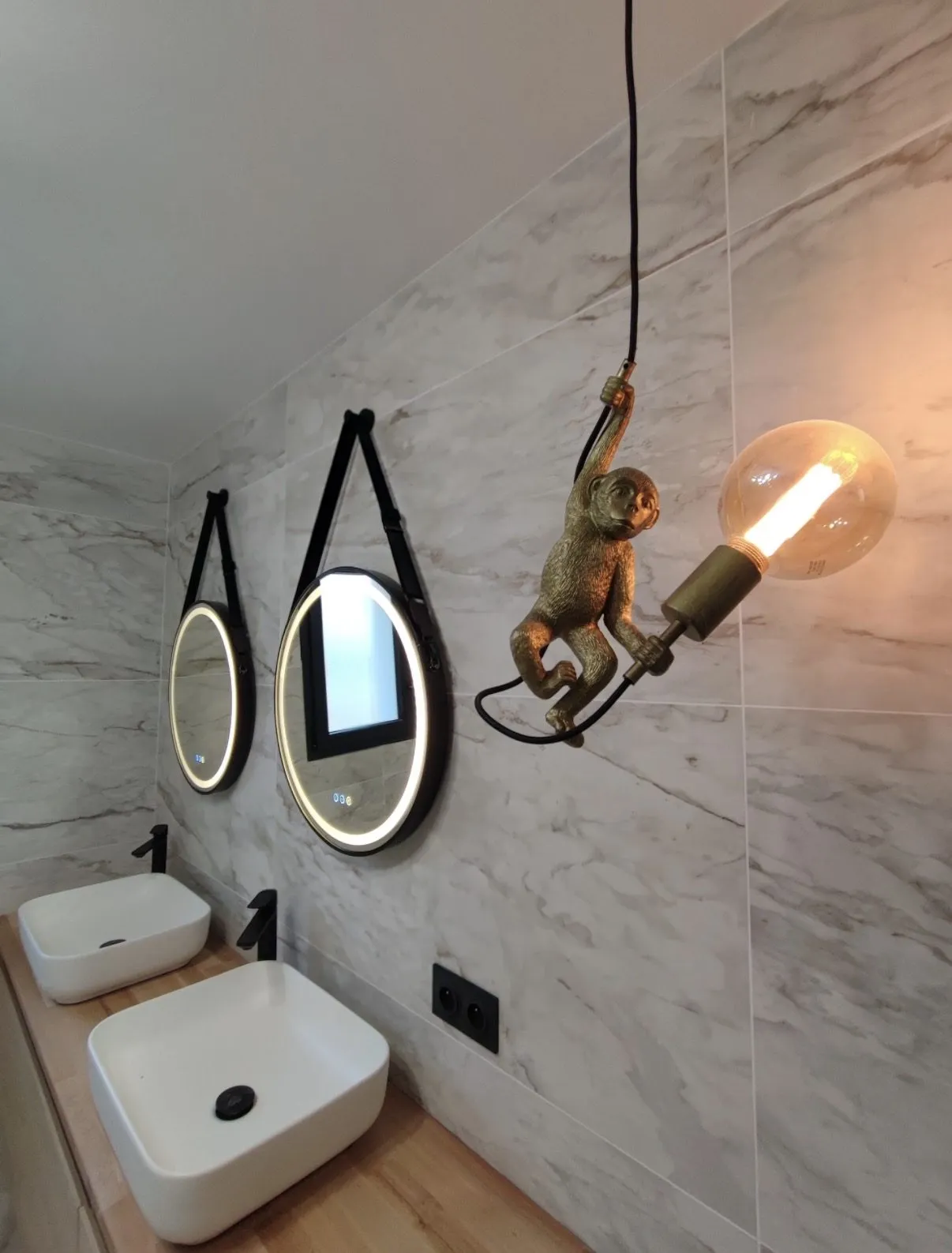 Détail d'une salle de bains : double vasque carrée sur plan chêne, miroirs ronds rétroéclairés suspendus et applique laiton