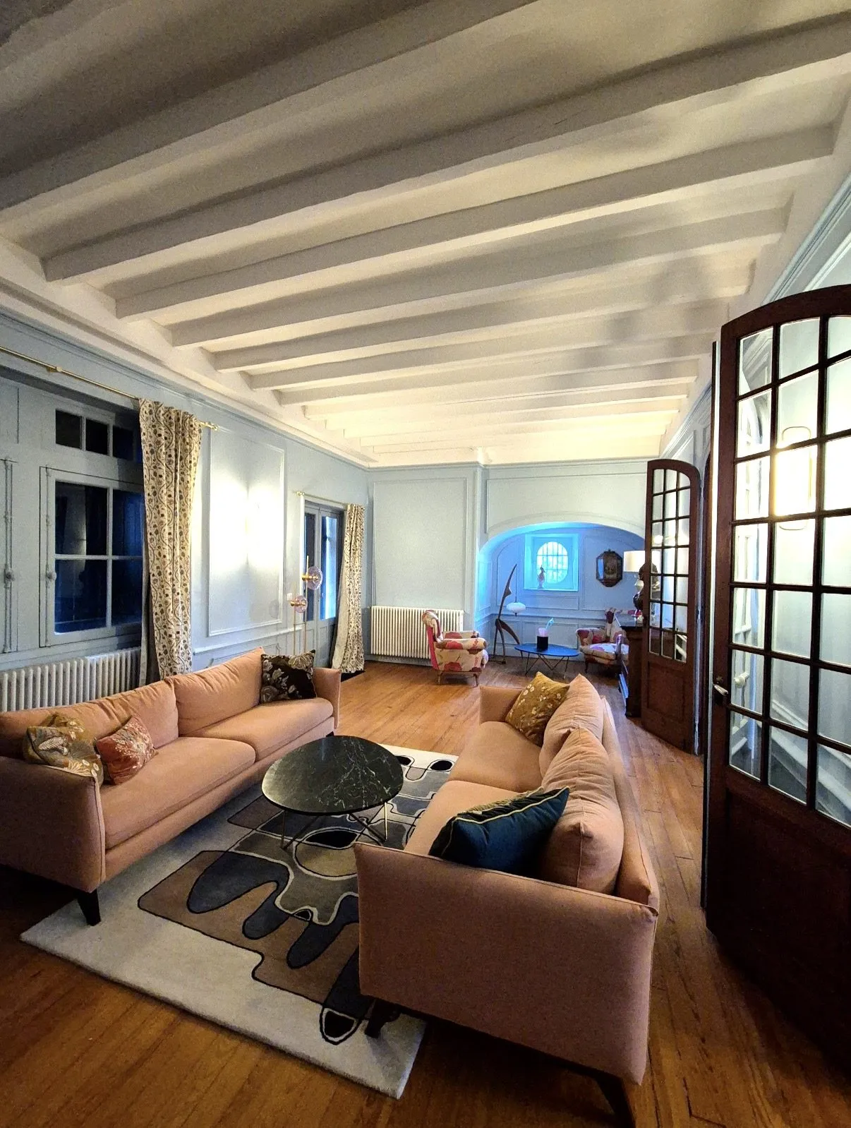 Salon de maison ancienne avec poutres blanchies, boiseries, parquet et double porte vitrée